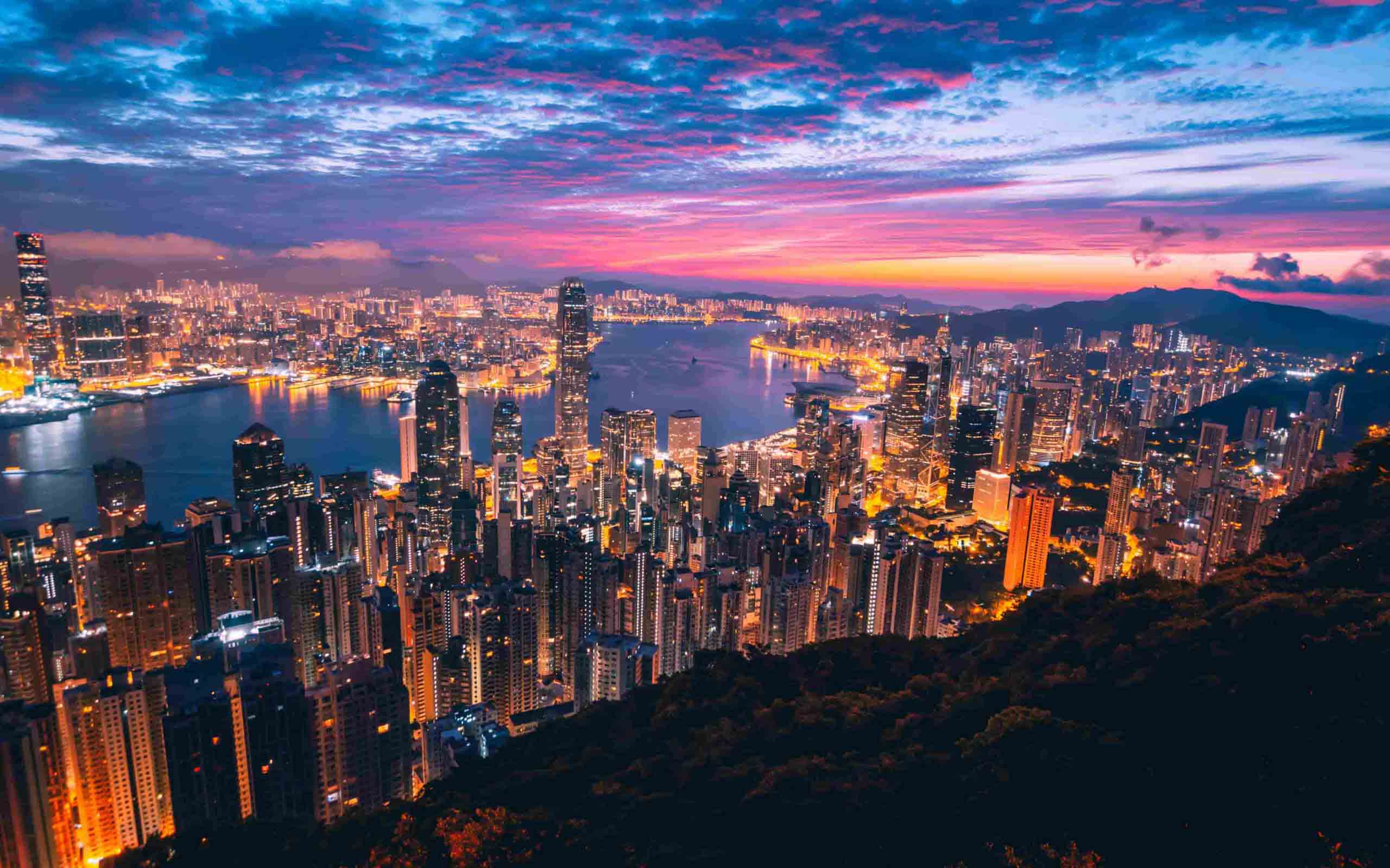 A baía Victoria Harbour de Hong Kong com os arranha-céus iluminados ao entardecer
