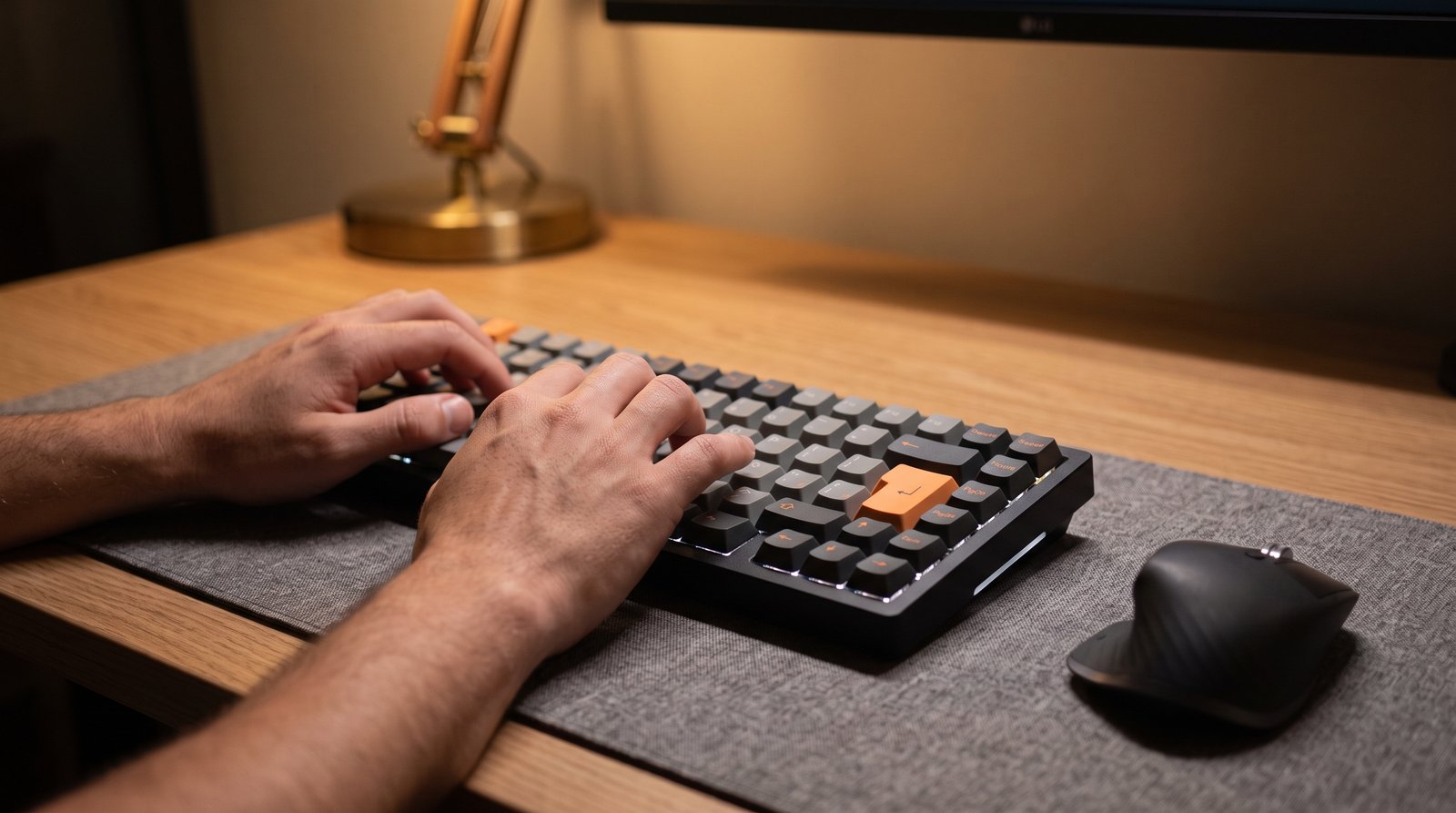Mãos digitando num teclado mecânico iluminado sobre mesa de trabalho, com mouse e tapete de mesa ao lado